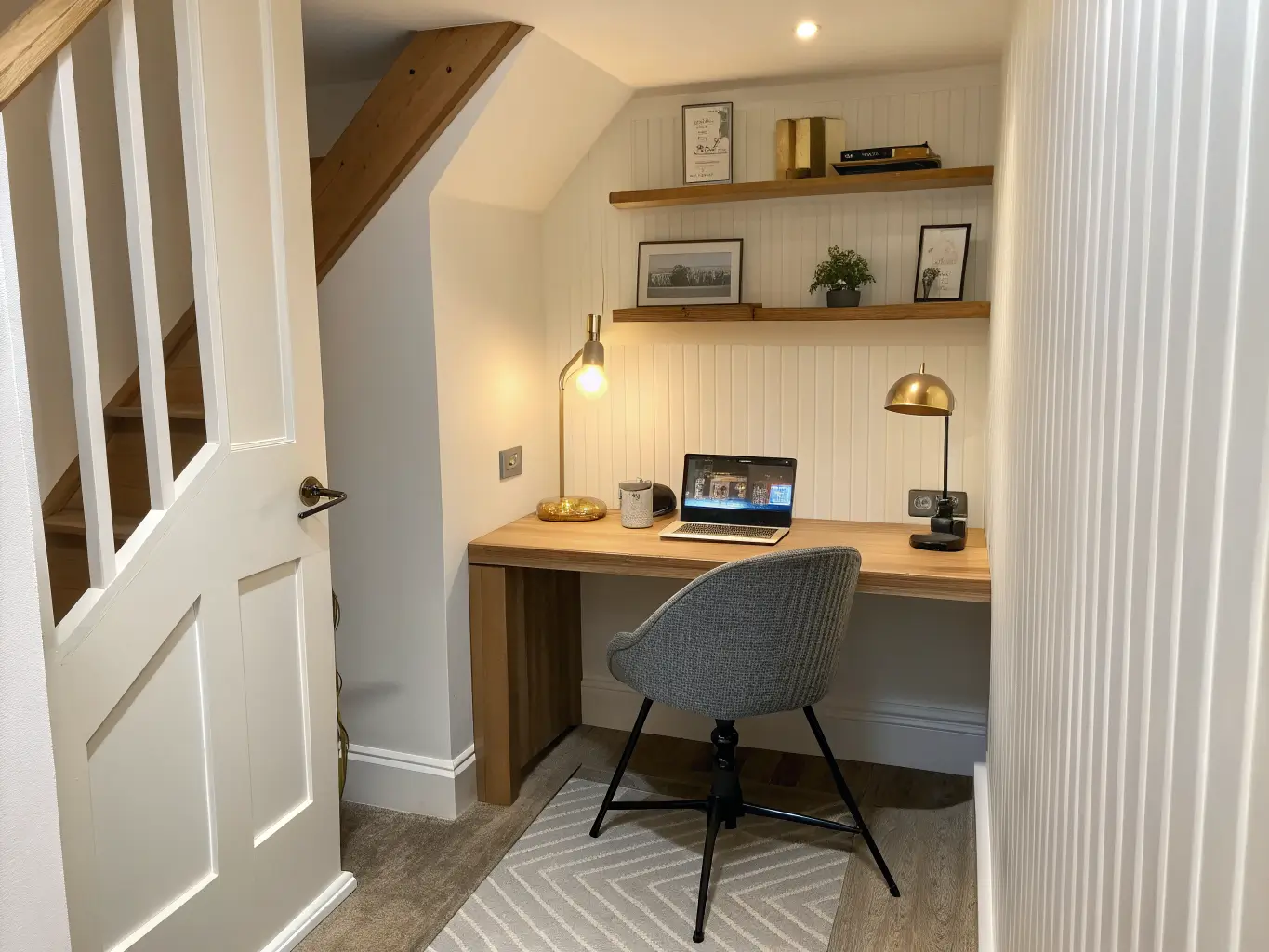 Photorealistic hallway alcove study nook with wall-mounted light oak desk, grey ergonomic chair, cream walls with vertical wood slat panel, warm task lamp, and pothos on a shelf.