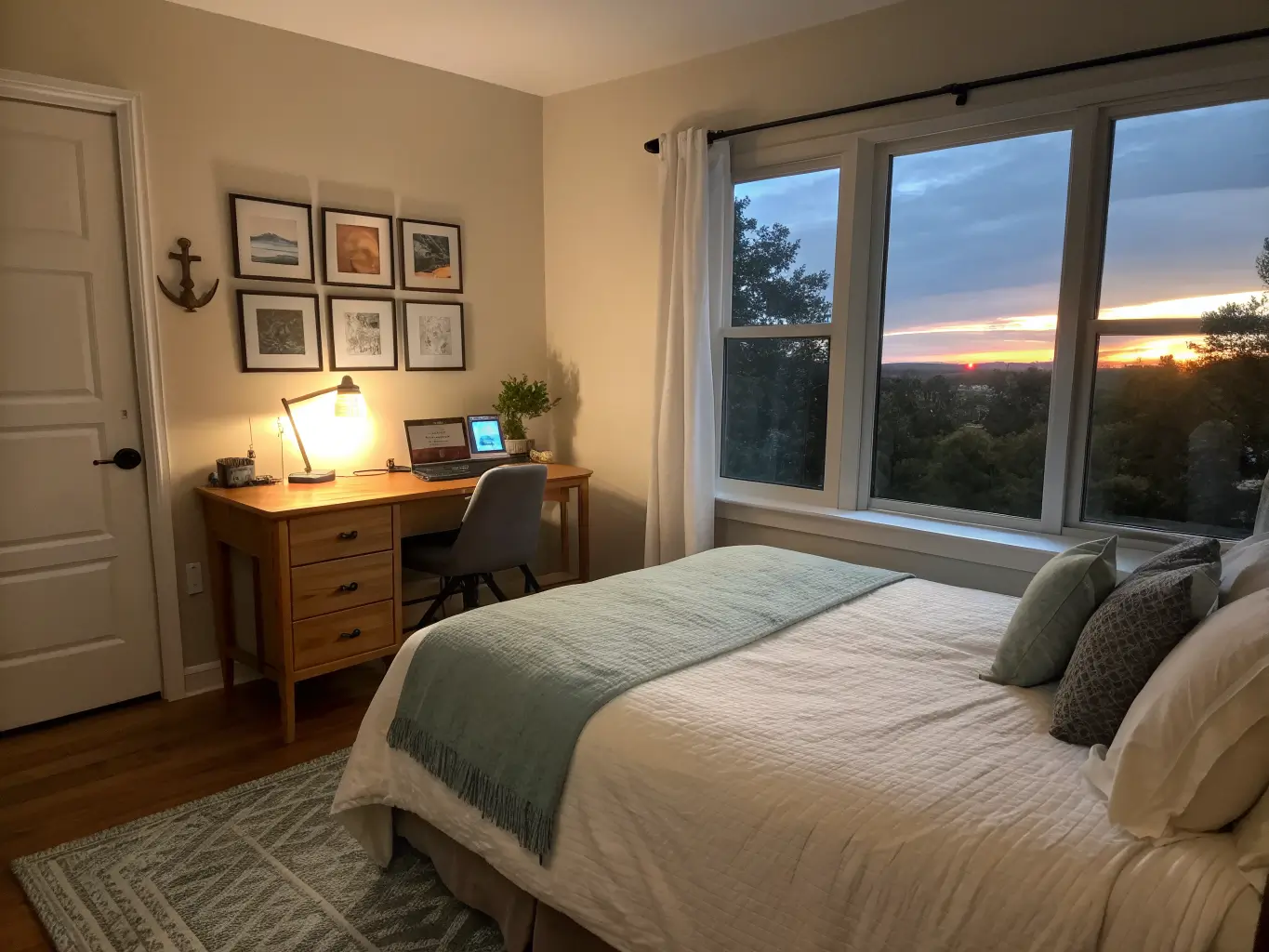 Side-angle dusk view of a cozy bedroom with a bed in the foreground, a desk under a window lit by fading daylight and a warm lamp, and a framed artwork beside the desk.